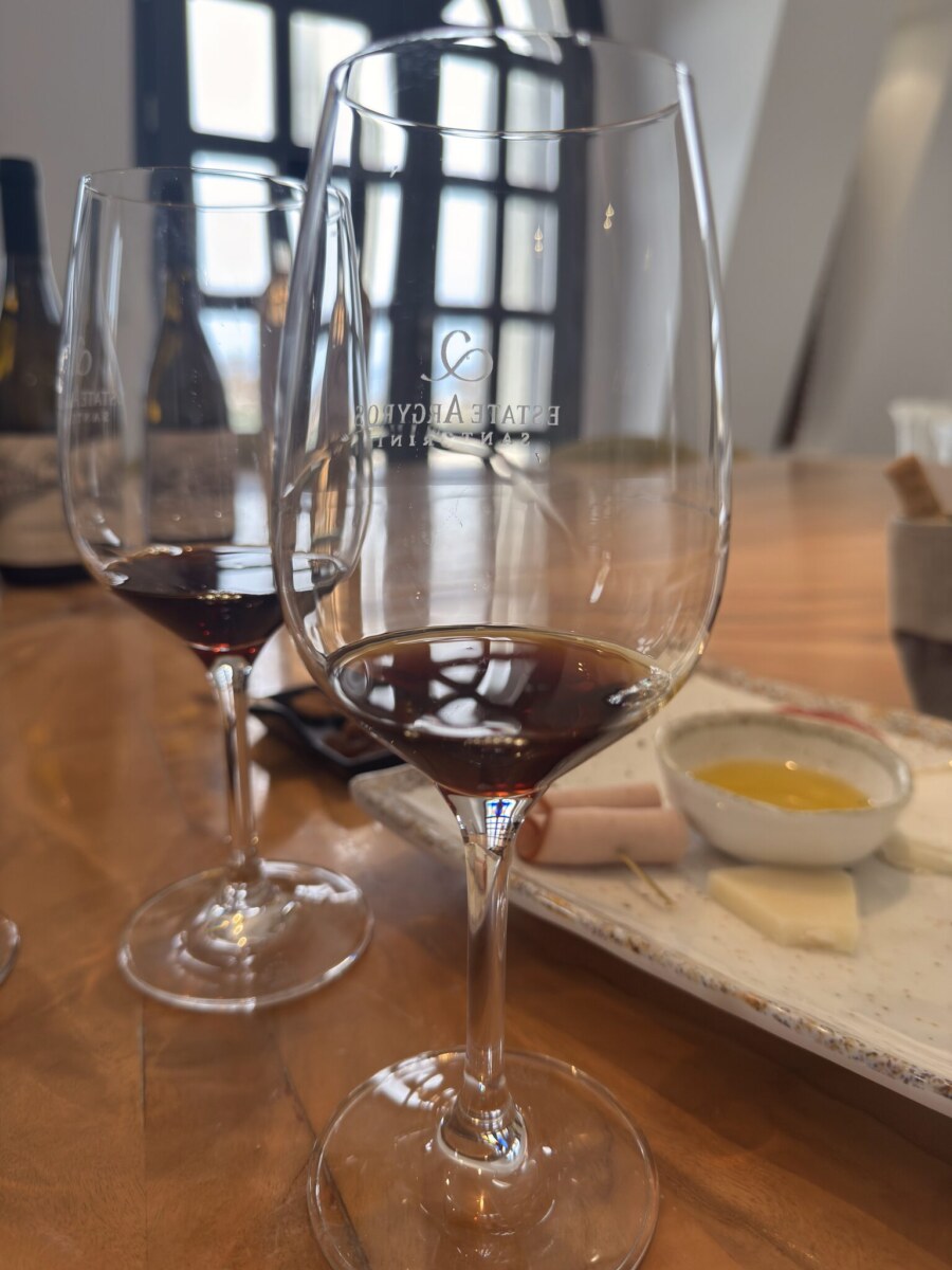 Etched Estate Argyros crystal wine glass filled with mahogany-amber Vinsanto dessert wine alongside cheese pairing.