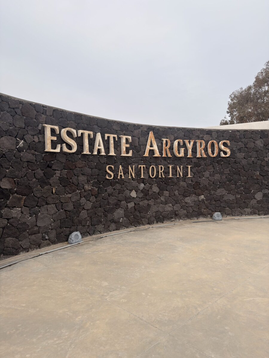 Volcanic stone entrance wall with Estate Argyros Santorini metal signage in Episkopi Gonia.
